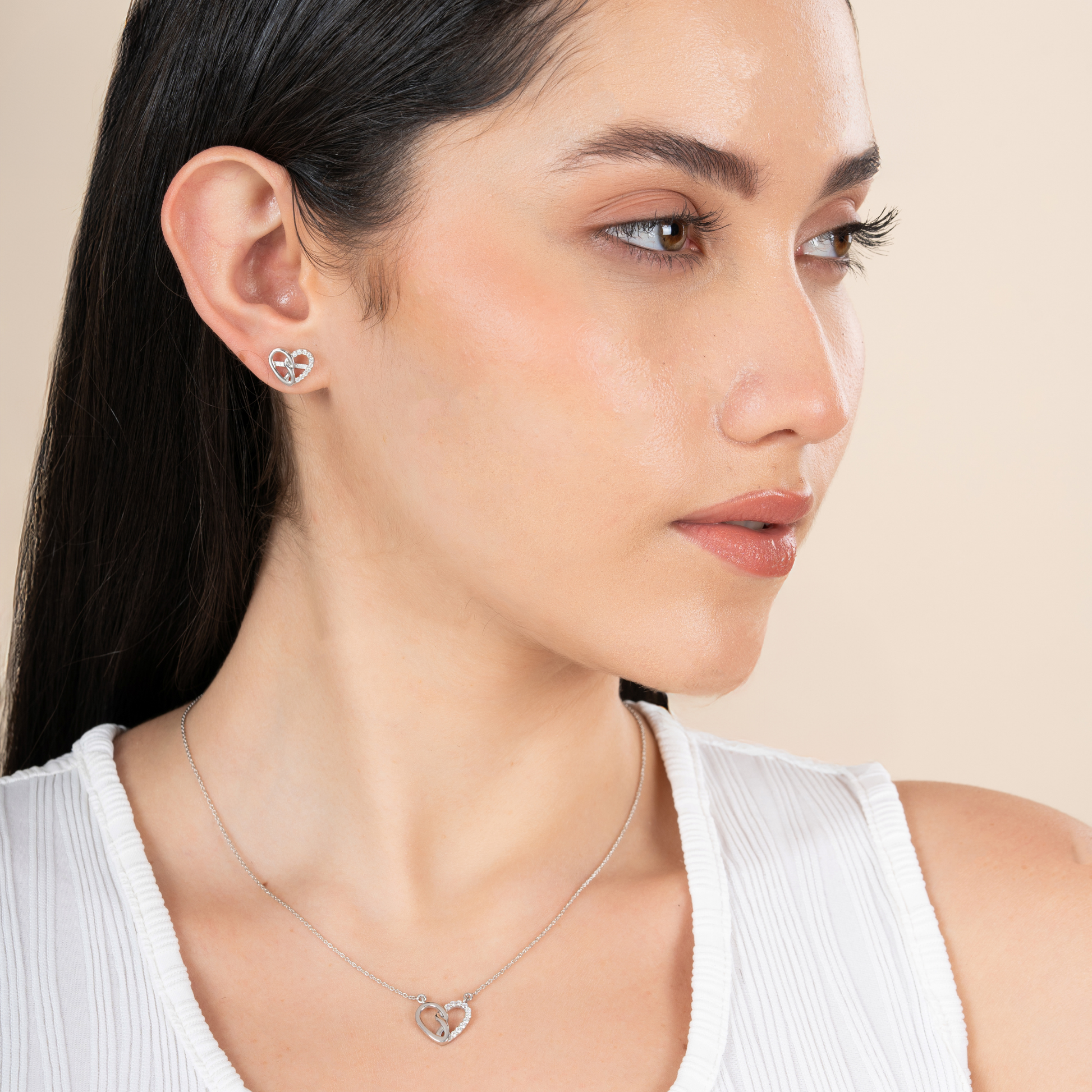 Woman wearing a heart-shaped earring and necklace on a beige background