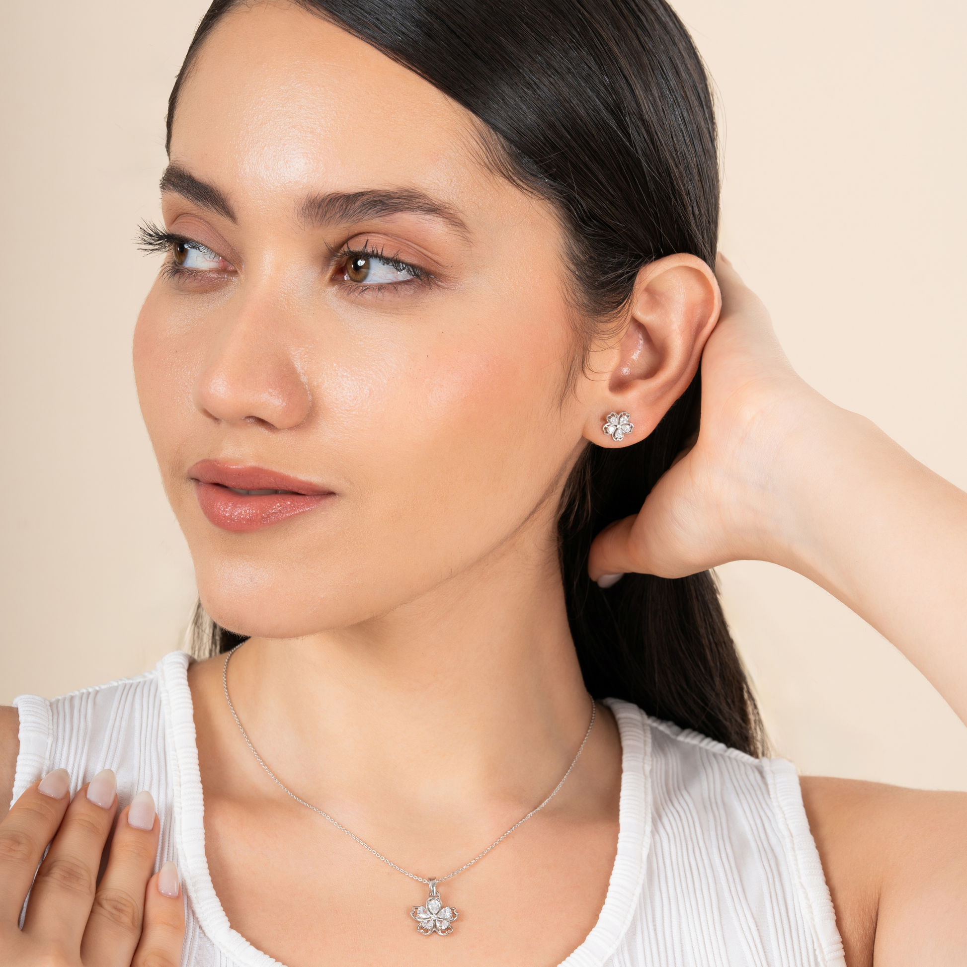 Woman wearing diamond earrings and necklace against a beige background